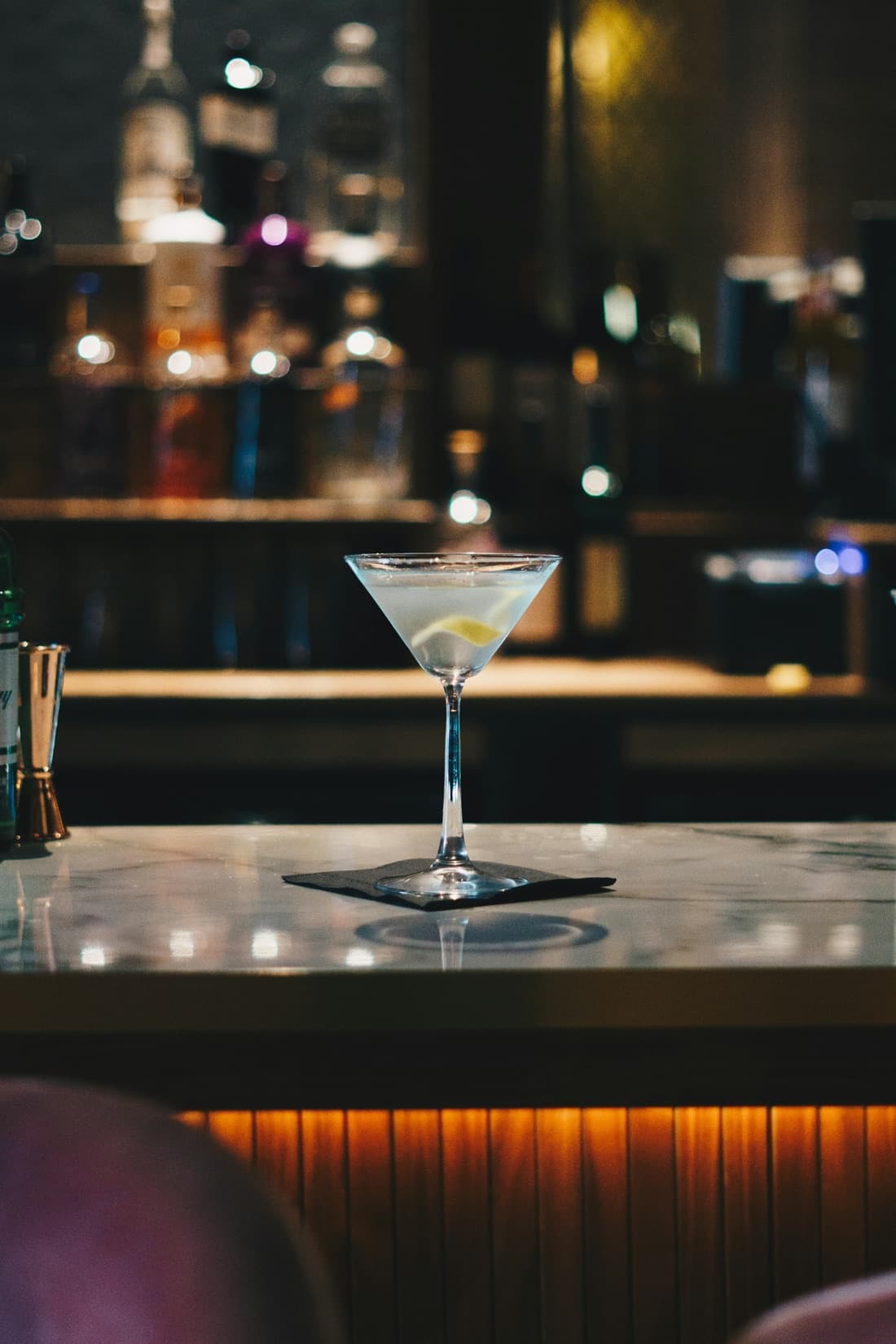 Cocktail servi dans une coupe, lumières tamisées du bar.